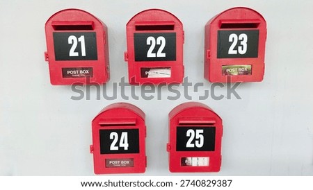 Row of red mailboxes numbered 21 to 25 mounted on white wall, symbolizing residential mail delivery, apartment correspondence system and urban housing communication. 