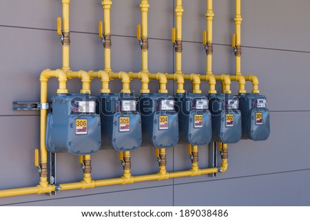 Row of residential natural gas meters and yellow pipe plumbing on exterior wall to measure household energy consumption
