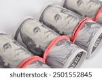 A row of rolled hundred dollar bills with rubber bands isolated on white background, stack of one hundred dollars American cash money bills rolled up with rubber band.