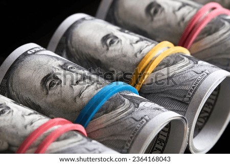 A row of rolled hundred dollar bills with rubber bands on dark background
