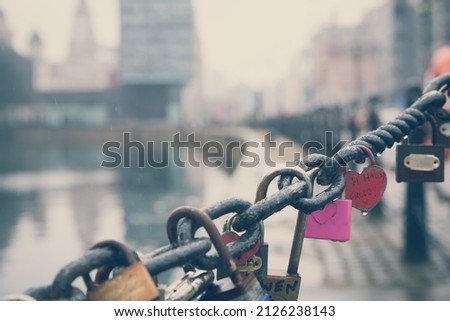Row of romantic good luck padlock charms on a chain link fence on a raining day beside Salthouse Dock in Liverpool in the United Kingdom