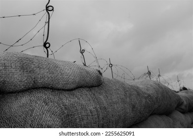 A row of sandbags on top of a WW1 trench with barbed wire over the top. black and white