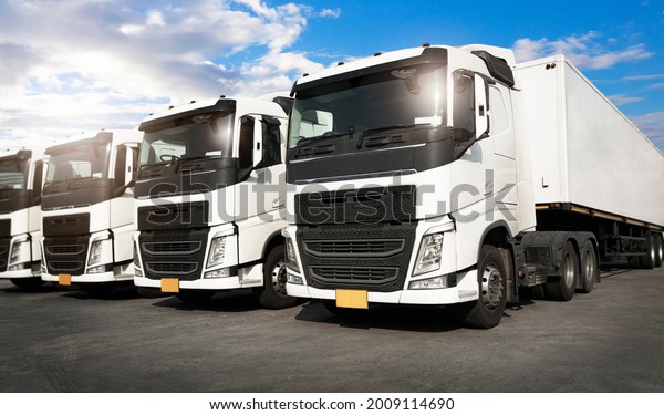 Row of\
Semi Trailer Trucks Parking at a Blue Sky. Industry Road Freight by\
Truck. Logistic and CargoTransport\
concept.