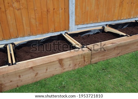 Row of separate raised flower beds or planters, or vegetable boxes. Compost fill. Edged with wooden railway sleepers. Domestic back garden. Outdoors on a spring day. Outdoor leisure or hobby activity