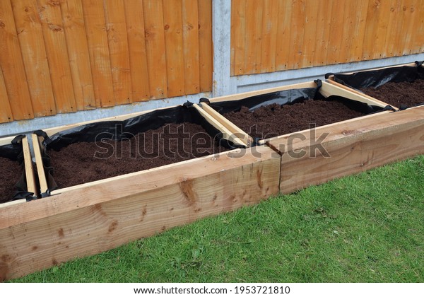 Row of separate raised flower beds or planters,\
or vegetable boxes. Compost fill. Edged with wooden railway\
sleepers. Domestic back garden. Outdoors on a spring day. Outdoor\
leisure or hobby activity