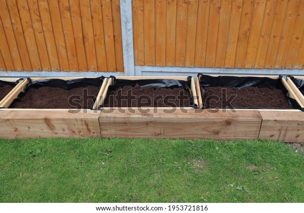 Row of separate raised flower beds or planters,\
or vegetable boxes. Compost fill. Edged with wooden railway\
sleepers. Domestic back garden. Outdoors on a spring day. Outdoor\
leisure or hobby activity