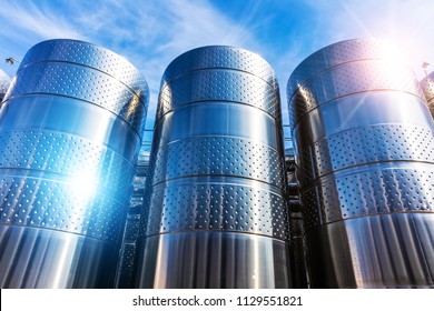 Row Of The Shiny Stainless Steel Storage Tank Containers At The Chemical Plant Factory Against Blue Sky With Clouds