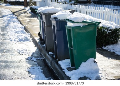 Row Of Snow Covered Compost, Recycle, And Garbage Dumpsters Along A Street Curb, In Winter Trash Pick Up Background