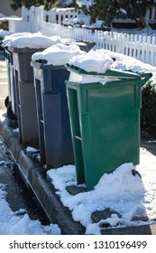 Row Of Snow Covered Compost, Recycle, And Garbage Dumpsters Along A Street Curb, In Winter Trash Pick Up Background