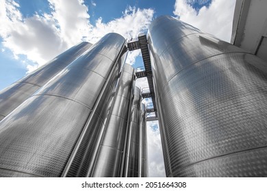 A row of stainless steel fermentation wine tanks against clouds and a blue sky. Steel wine tanks for wine fermentation at a winery. modern wine factory with large shine tanks for the fermentation. - Powered by Shutterstock