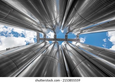 A row of stainless steel fermentation wine tanks against clouds and a blue sky. Steel wine tanks for wine fermentation at a winery. modern wine factory with large shine tanks for the fermentation.