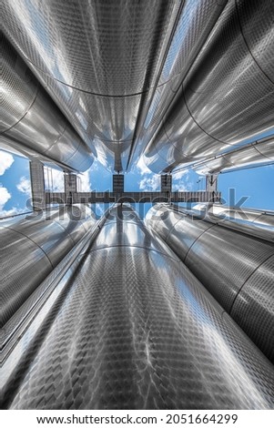 A row of stainless steel fermentation wine tanks against clouds and a blue sky. Steel wine tanks for wine fermentation at a winery. modern wine factory with large shine tanks for the fermentation.