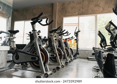 A row of stationary bikes are lined up in a gym. The bikes are all different colors and sizes, and they are all in use. The gym is well-lit and has a modern, sleek design - Powered by Shutterstock