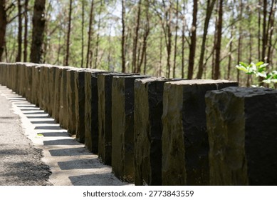 A row of stone pillars casts angled shadows along a quiet forest path.
