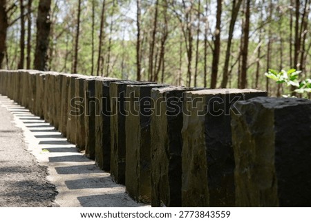 A row of stone pillars casts angled shadows along a quiet forest path.