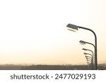 A row of street lights against the golden sky sunset. The street lamp post on the way. Urban electro-energy technologies.