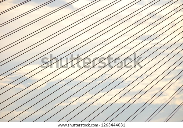 A row string steel cables of a bridge\
against blue sky white clouds in bright day\
