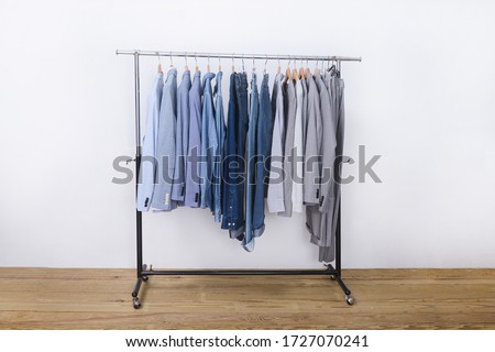 Row of suit blue striped shirt with blue , gray ,white long sleeved shirts with blue jeans.gray pants on hanger-wooden background 
