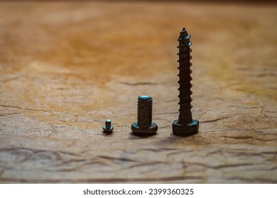 A row of three fasteners for fixing different construction materials, with increasing length on a red, uneven surface close-up.