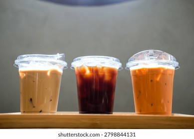 A row of three refreshing iced latte, iced Americano and an iced Thai milk tea served on wood tray