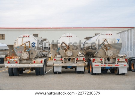 Row of three shiny metal tanker trucks used to transport fuel.