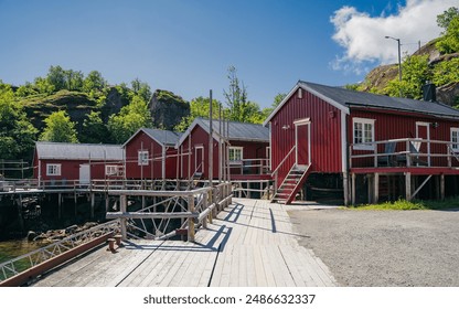 A row of traditional red wooden cabins on stilts lines a wooden boardwalk in a picturesque Norwegian fishing village. Idyllic beauty and timeless appeal of coastal Scandinavian life - Powered by Shutterstock