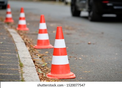 A row of traffic cones standing on a street along the curbstone of the pavement to prevent other people from parking their cars there. Seen in Germany