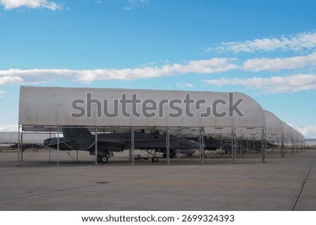Row of twin-engine multirole fighters aligned under maintenance covers on a military apron