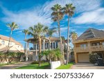 Row of two-story beach house vacation home rental property with porch, clay tile roofs with line of palm trees under sunny cloud blue sky near downtown South Padres Island, travel destinations. USA