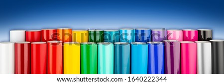 Row of various rainbow colored vinyl car wrapping or plotter cutting sticker foil film rolls on blue white wide panorama banner background