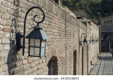 A row of vintage street lamps casts soft shadows against an aged brick wall, showcasing old-world charm and history in a serene setting. - Powered by Shutterstock