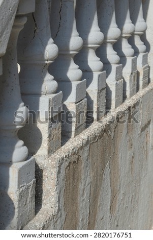 A row of weathered grey concrete balusters forms a decorative railing on top of a textured stone retaining wall casting strong shadows