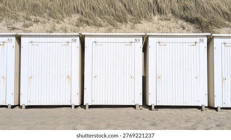 Row of white beach cabins on a sandy Dutch North Sea coast, with grass dunes and blue sky. Minimal coastal architecture, North Sea, Netherlands summer. Clean composition with copy space. Horizontal banner.
Ideal for illustrating beach rental huts, oceanfront recreation, summer weather, and vacation planning.