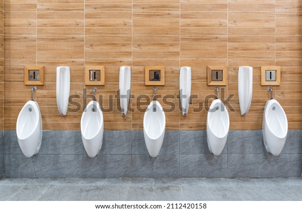 Row of white ceramic urinal chamber pot interior\
design with beautiful ceramic wall panels imitating wood the men\
public toilet or restroom. Concept modern architectural decoration\
design.