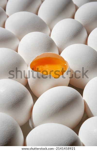Row of white eggs\
and single broken egg with a yolk. White Eggs and Yellow Egg\
Yolk.Shallow depth of field