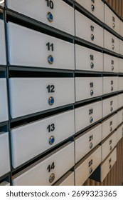 A row of white mailboxes with numbered slots. The mailboxes are metallic with blue knobs. The setting appears to be an indoor area, possibly an office or apartment building.