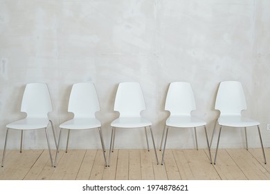 Row of white plastic chairs on metal legs placed on parquet against gray wall