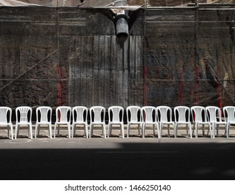 A Row Of White Plastic Chairs In The Street, Forward View. Empty Chairs Against A Granite Wall. Waiting Concept.