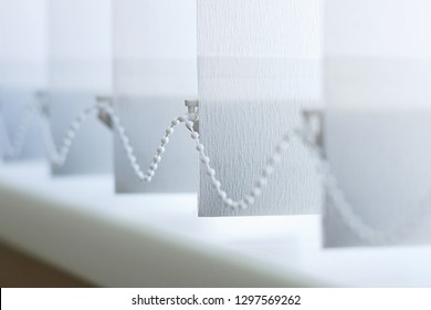 A row of white vertical blinds cover the sunlight from the window. Close up.