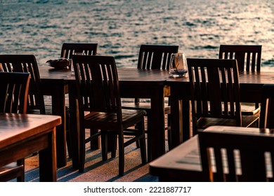 Row Of Wooden Tables And Chairs Of A Restaurant On The Beach Of Thailand, No People, Sunset Time, Blurred Background Of Sea Wave.