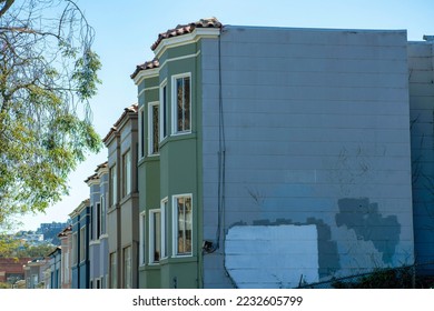 Row of worn down or aged multicolored apartment buildings or town homes in the downtown neighborhood of San Francisco California. In late afternoon shade with front yard trees in a suburban area.