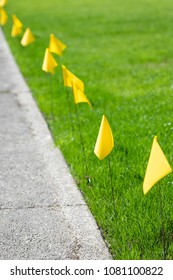 Row Of Yellow Marker Flags For A Buried Natural Gas Line In A Grass Lawn, Along A Concrete Sidewalk, With Space For Text On The Left 