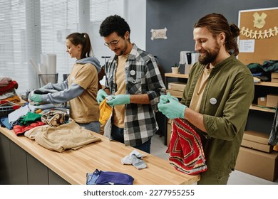 Row of young intercultural people sorting second hand clothes for those in need while standing by table in office of volunteering organization - Powered by Shutterstock