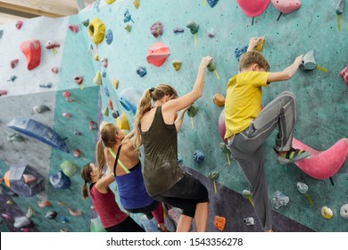 Row of young sportswomen and schoolboy in activewear creeping upon climbing wall while holding by small rocks - Powered by Shutterstock