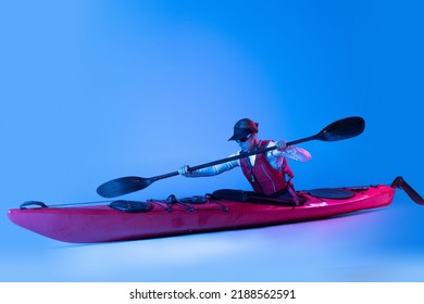 Rowing. Sportive woman in red canoe, kayak with a life vest and a paddle isolated on blue background in neon light. Concept of sport, nature, travel, active lifestyle