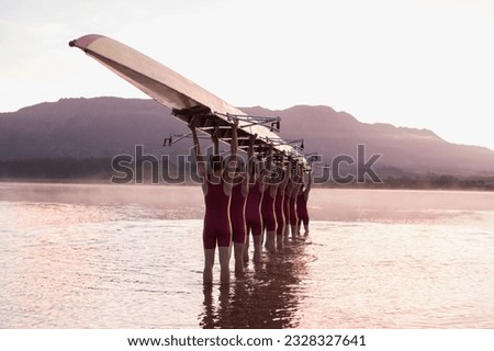 Rowing team carrying row boat overhead in still lake