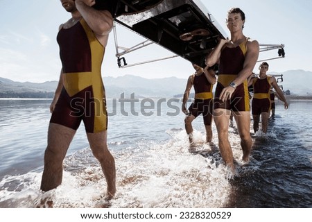 Rowing team carrying scull out of lake