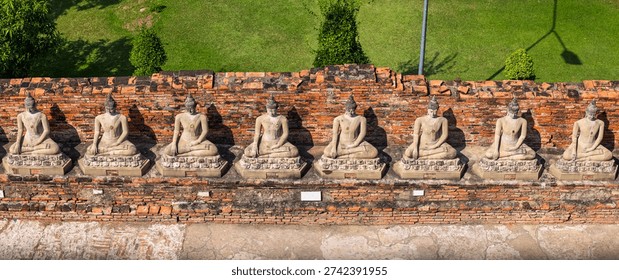 Rows of ancient Buddha statues sitting on a brick temple wall in Thailand