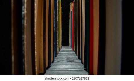 Rows Of Books With Colored Covers Arranged On Bookshelf In Library. Old Books With Red, Green And Blue Covers On Isolated Black Background With Dust Particles. Textbooks On Wooden Dark Table. Close Up