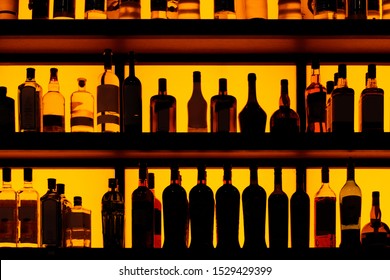 Reihen von Flaschen, die auf dem Regal in einer Bar sitzen, gelbe Hintergrundbeleuchtung